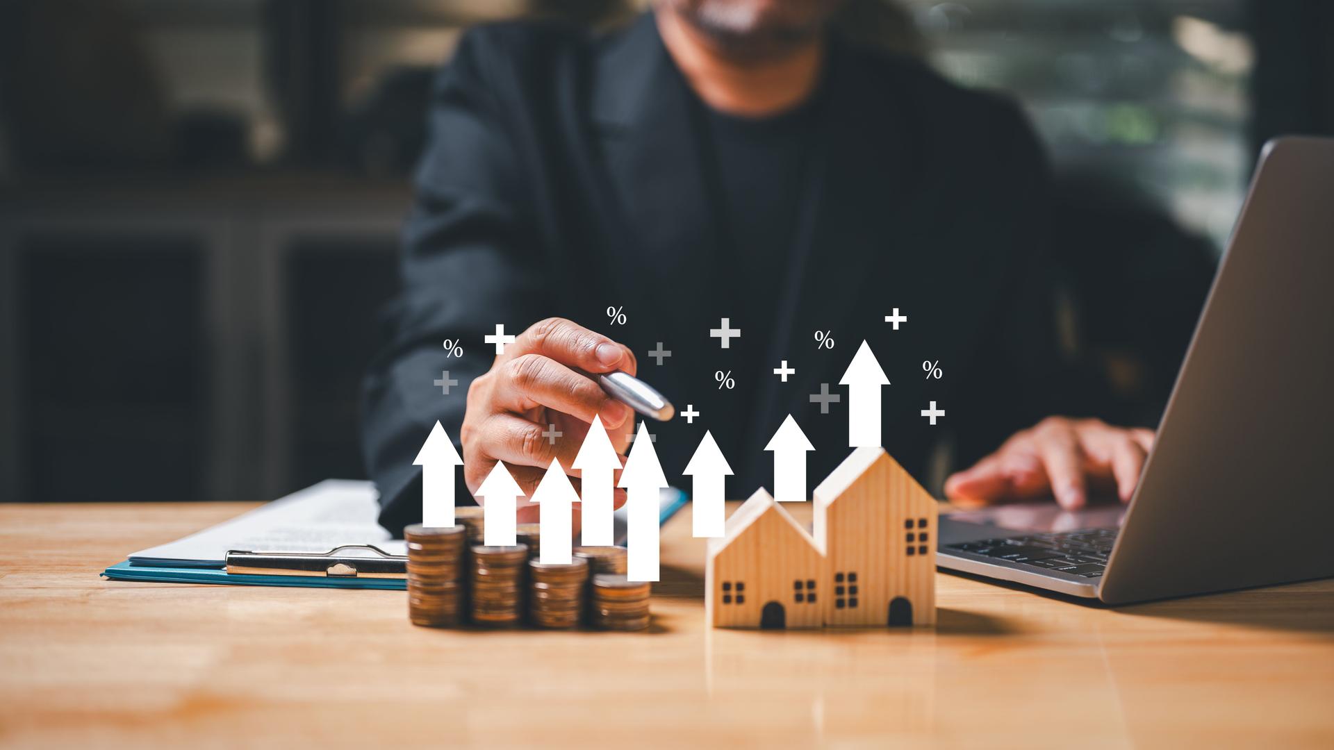 A businessman holding a coin in his hand ponders the concept of wealth and financial security as he looks at a house model, representing the potential investment of a mortgage loan.